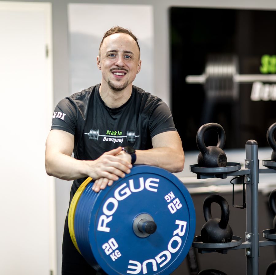 Andi lehnt lachend an einer Rogue-Hantelscheibe in seinem Studio