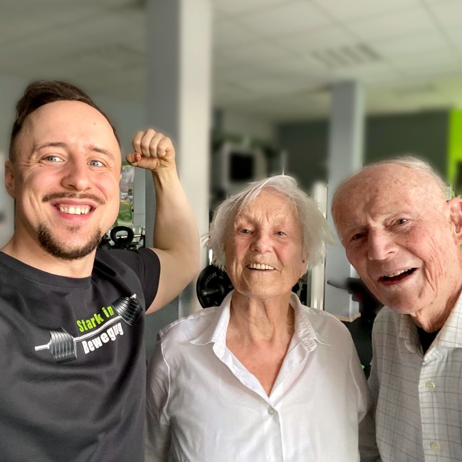 Andi zeigt lachend den Bizeps, neben ihm Sybille und Lutz, beide 90, im Studio