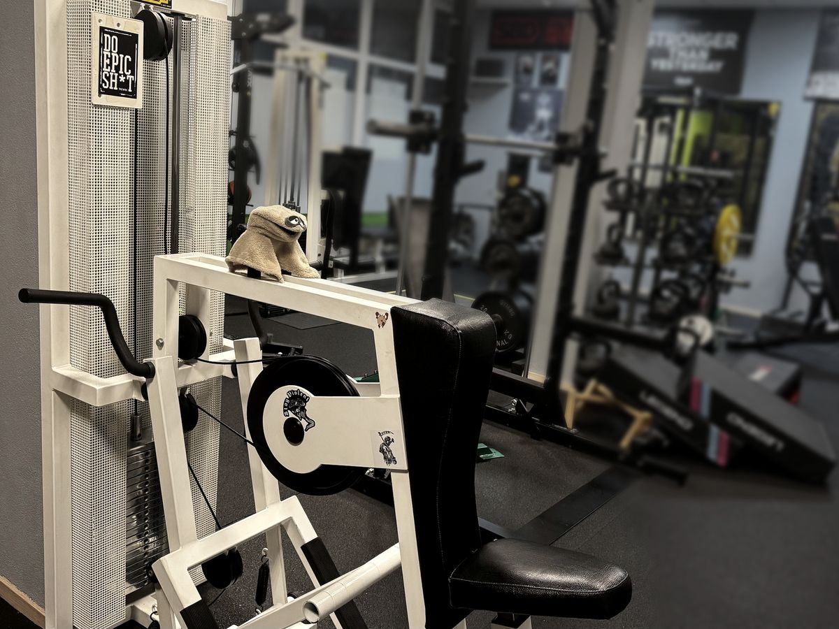 Blick ins Studio: weiße Technogym-Maschine vorne, dahinter Rack, Gym-80-Scheiben und Kettlebells